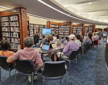 Students present to a group of new editors seated within the Auckland Museum library